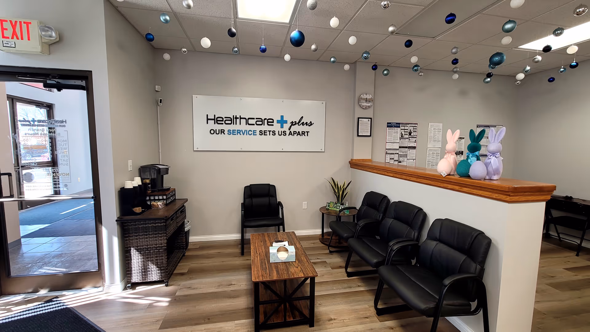 Lobby reception area with black chairs, a wooden counter, and a Healthcare Plus sign.