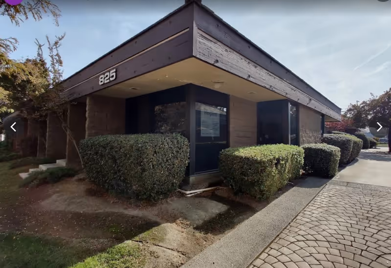 Single-story building entrance with address 825 and manicured hedges outside.