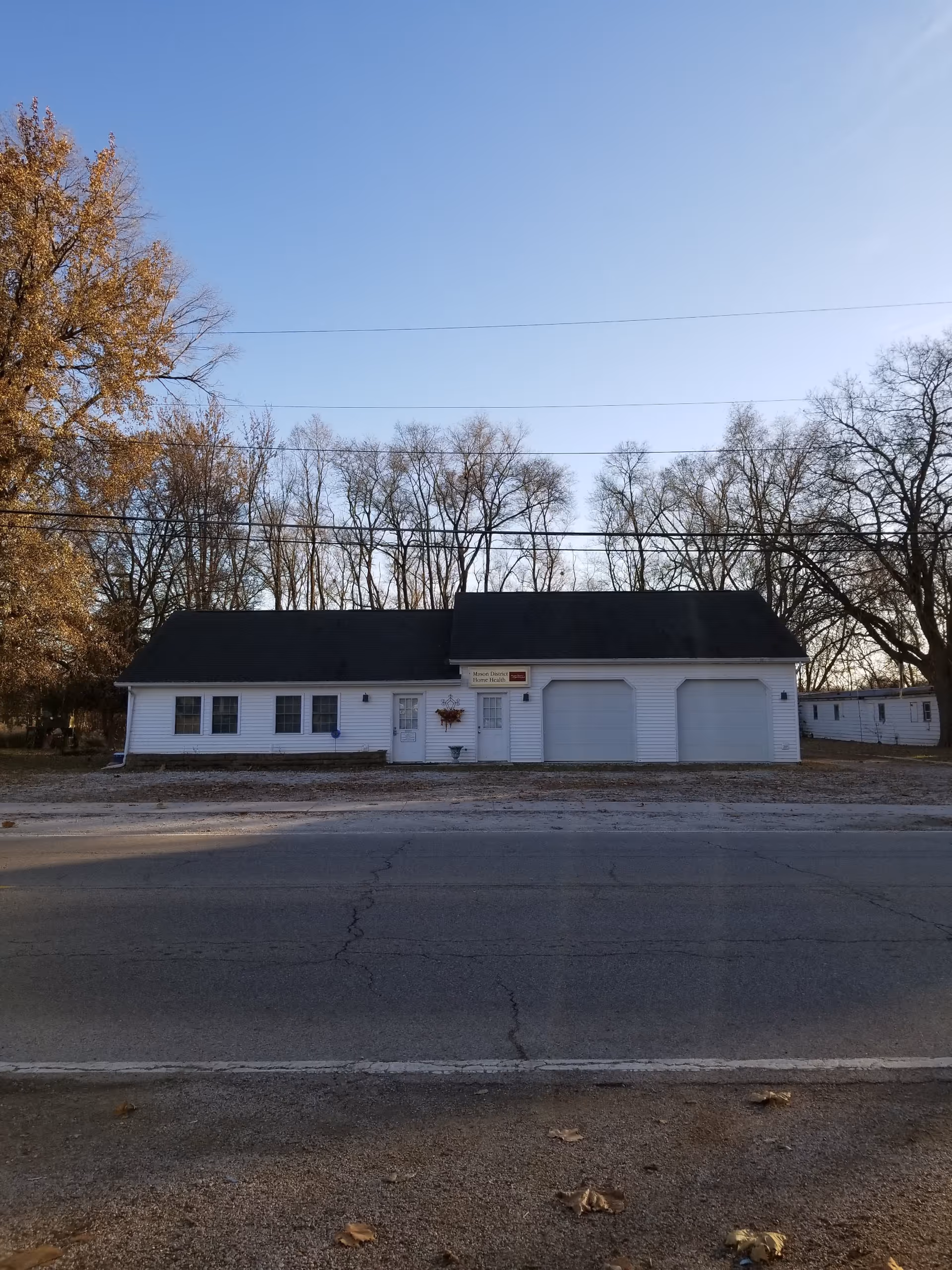 White, single-story building with two garage doors and leafless trees in fall