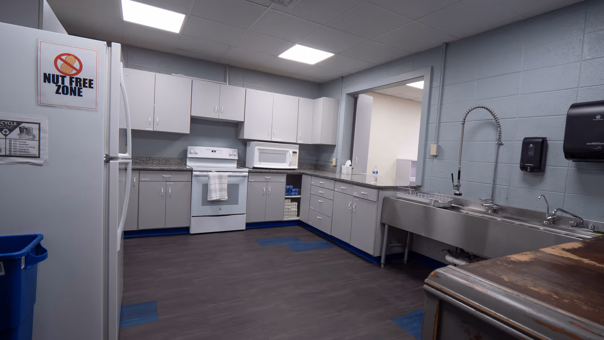 Industrial style communal kitchen with white cabinets, appliances, and a large stainless steel sink.