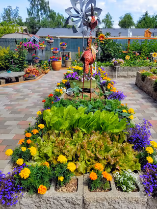 Colorful raised garden beds with flowers and a decorative wind sculpture in Apple Blossom Manor courtyard.