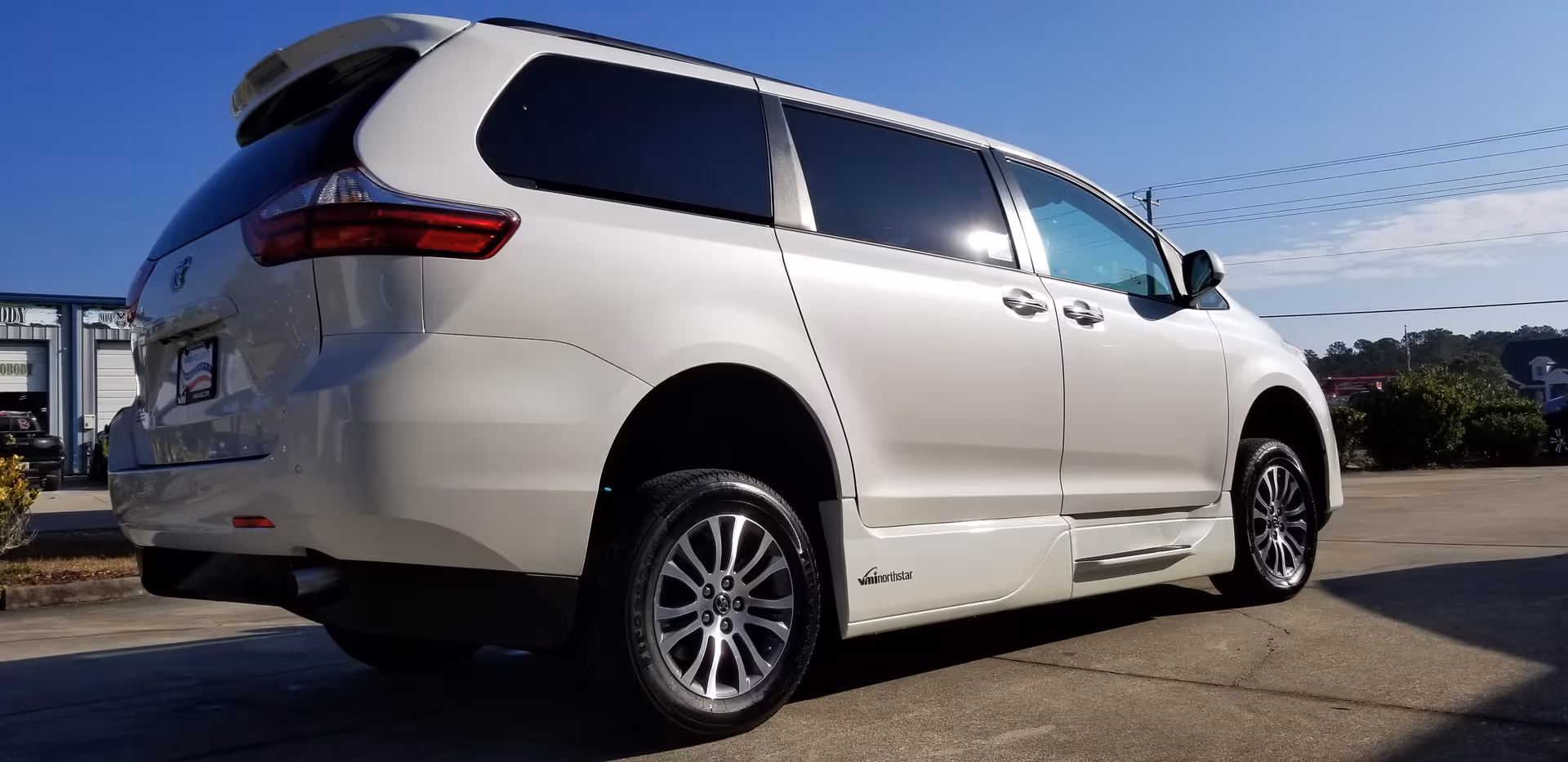 White minivan parked in a lot beneath a blue sky.