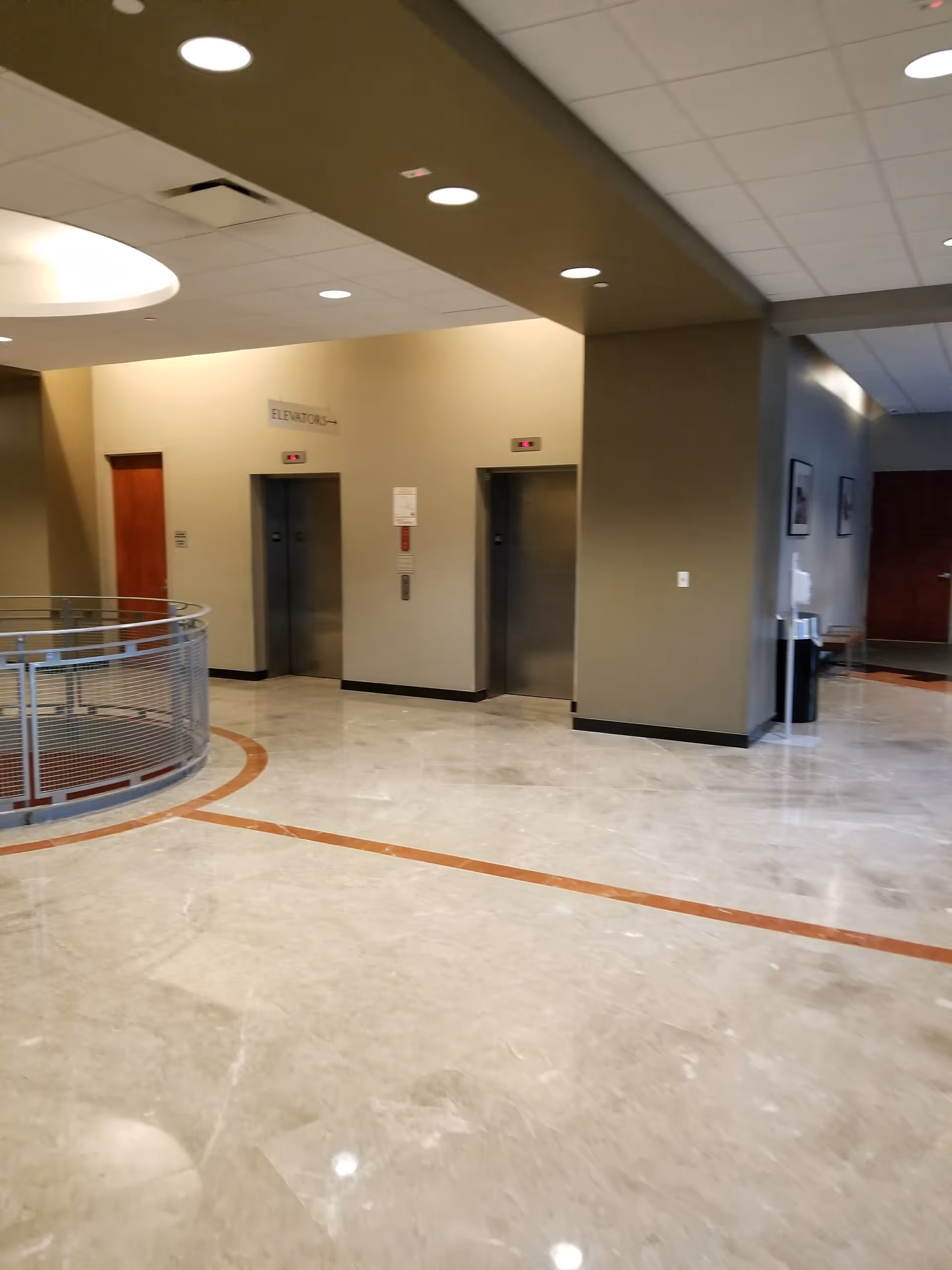 Modern interior lobby with two elevators, curved railing, and polished marble floor.