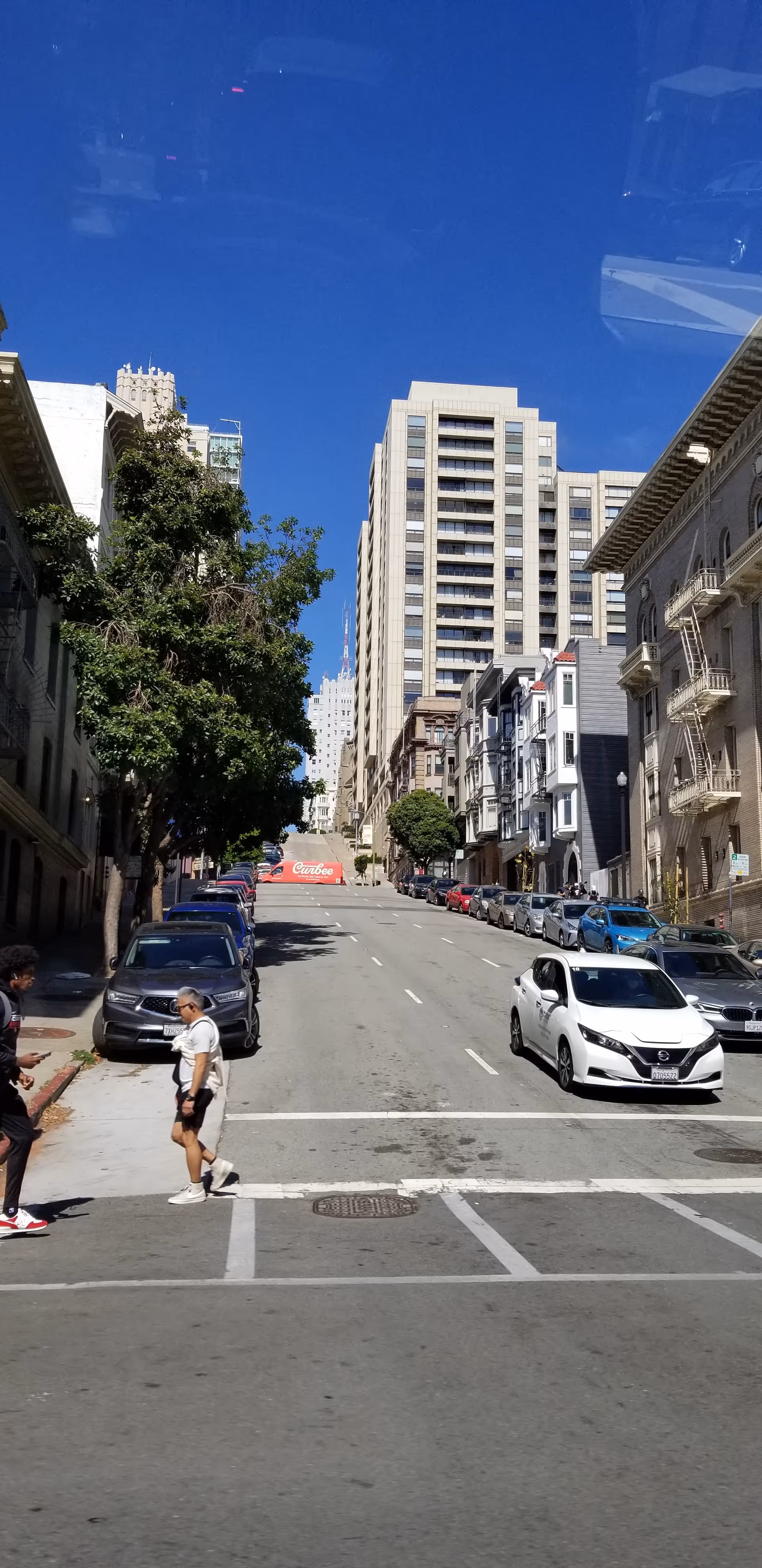 Urban San Francisco street scene with tall buildings, parked cars, and pedestrians.