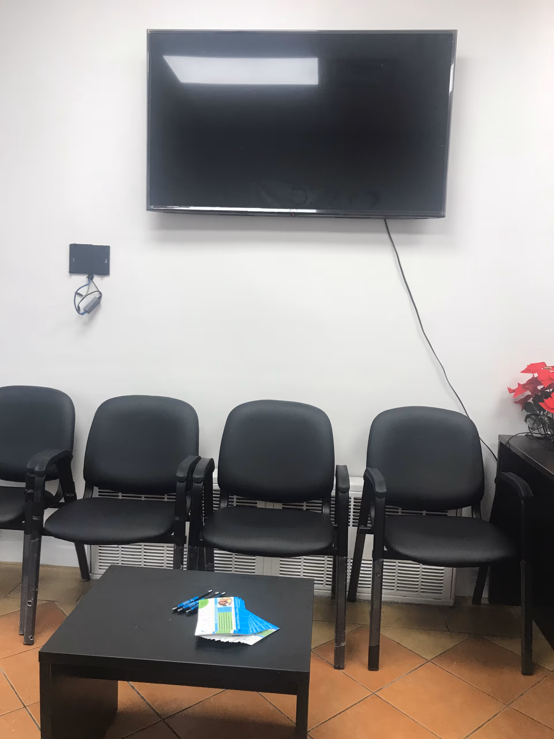 Waiting area with a wall-mounted flat-screen TV, lined chairs, and a small coffee table.