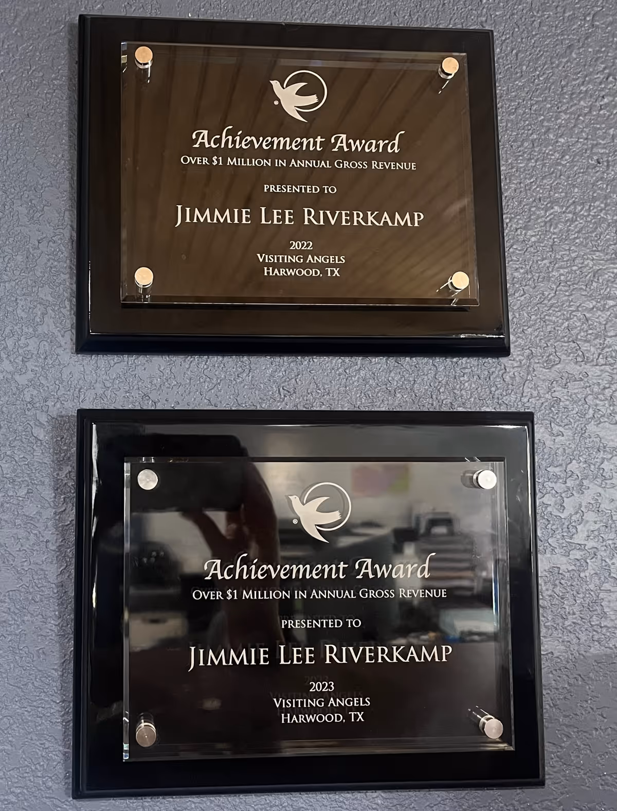 Two glass-framed achievement plaques mounted on a blue textured interior wall.