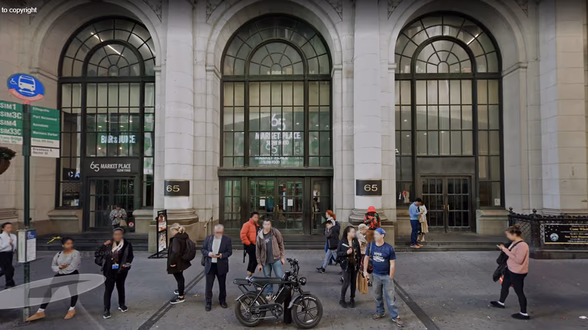 People stand outside a grand building with arched windows and tall columns on a city street.