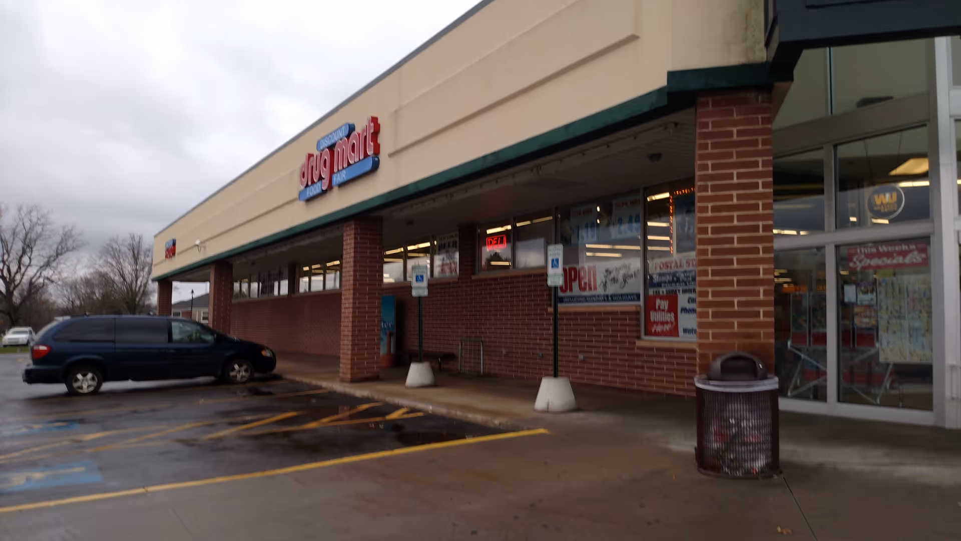 Exterior front of Discount Drug Mart with brick columns and parked blue van.