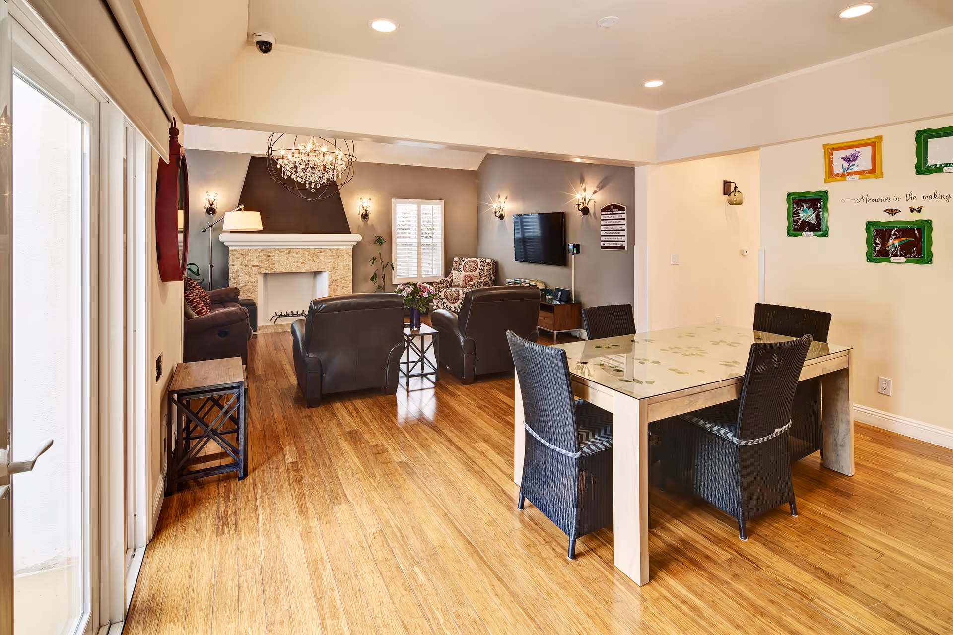 Bright senior living common area with fireplace, chandelier, and glass-topped dining table.