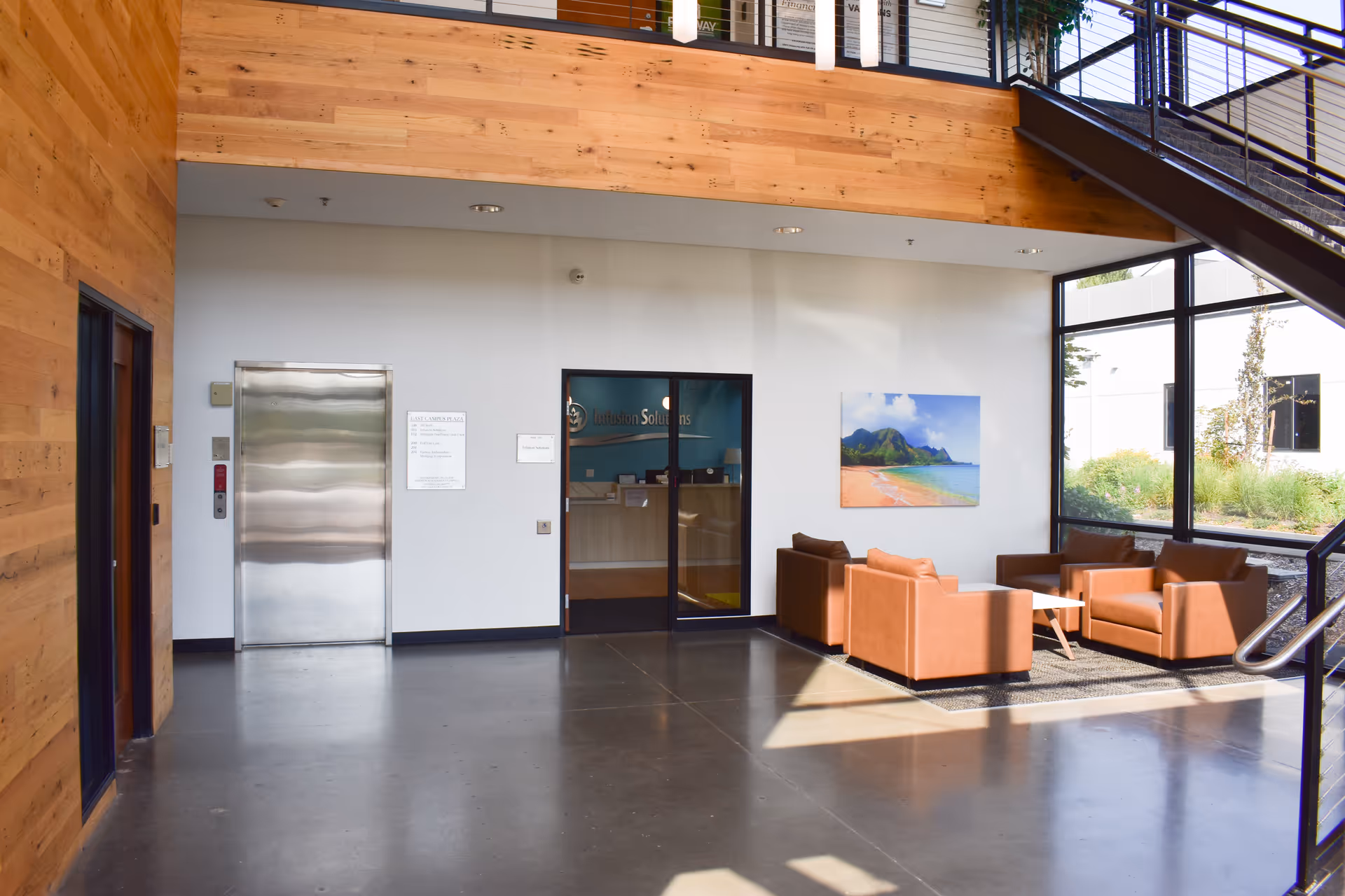 Spacious modern lobby with orange chairs, glass doors, elevator, and wooden wall accents.