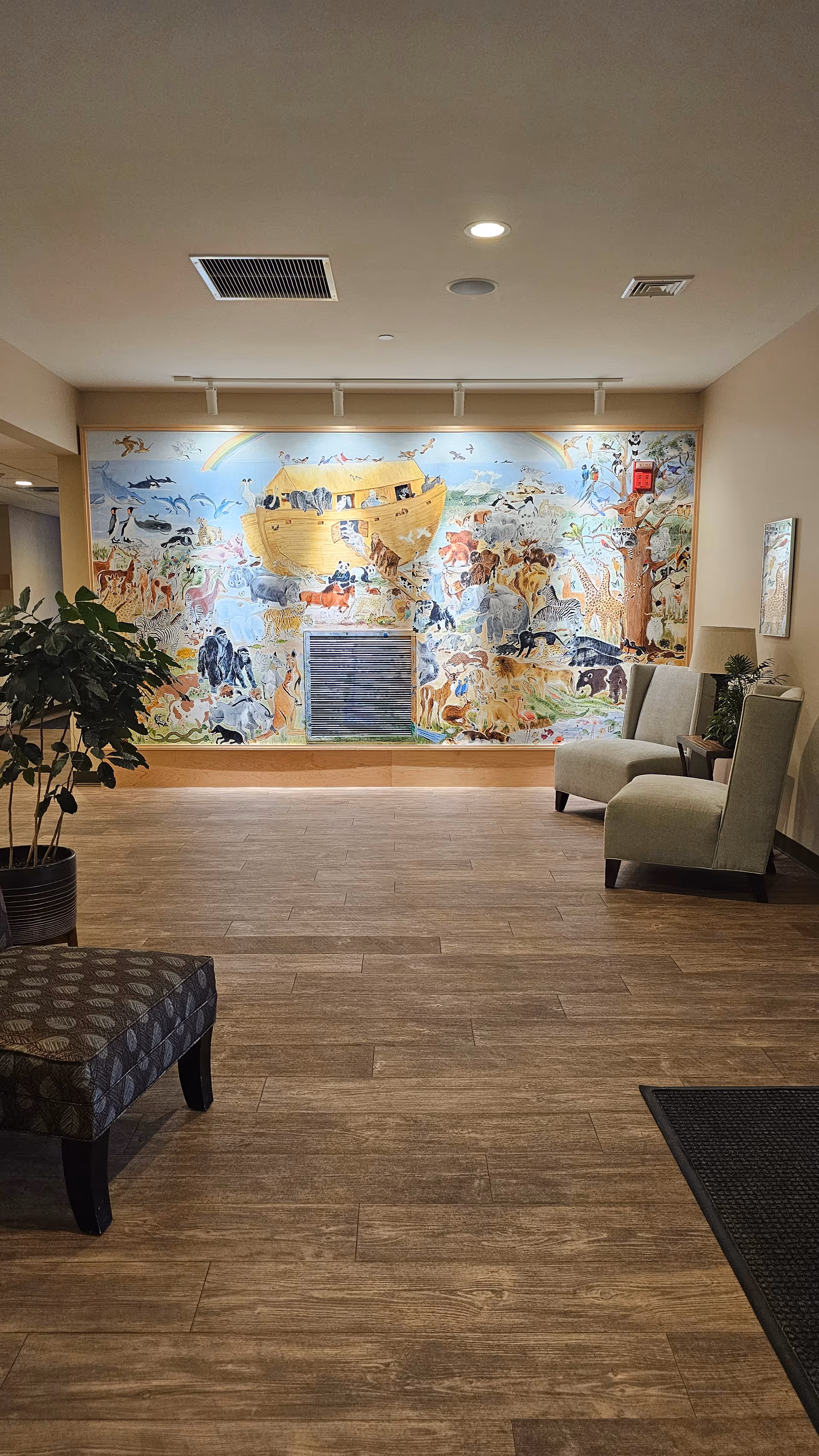 Interior lobby with a large colorful mural, two chairs, a plant, and wood flooring.