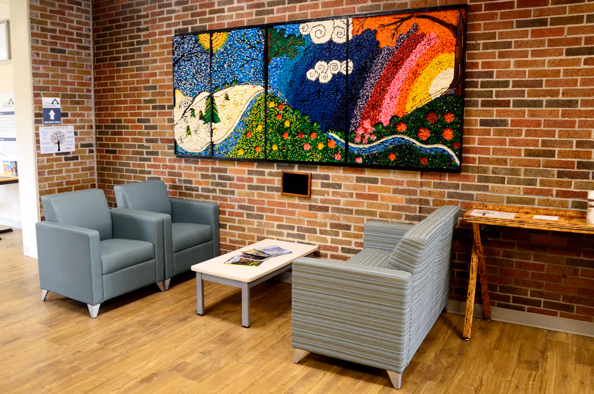 A brick-walled lounge with blue armchairs, striped chair, coffee table, and colorful wall art.