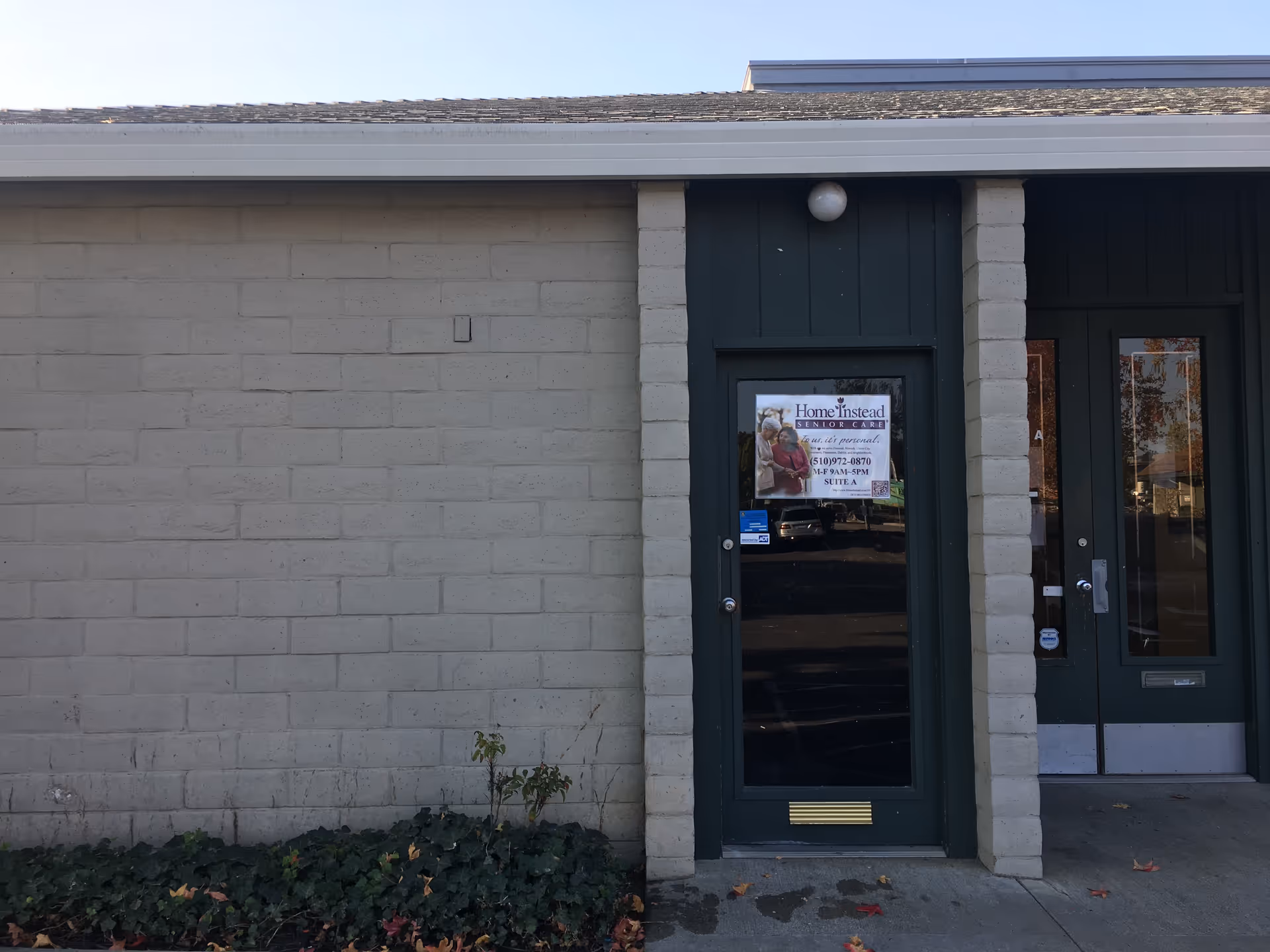 Front exterior of a beige brick building with a dark green door and a windowed entrance.