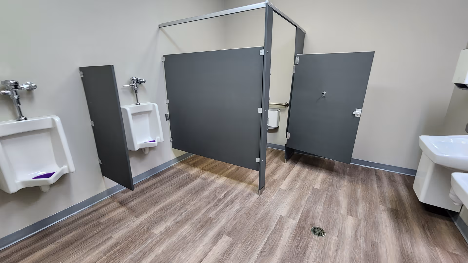 Senior living facility restroom with stalls, sinks, and wood-look flooring.