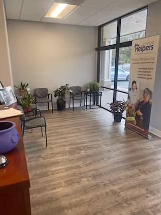 An interior waiting lobby with chairs, potted plants, and a Senior Helpers banner by windows.