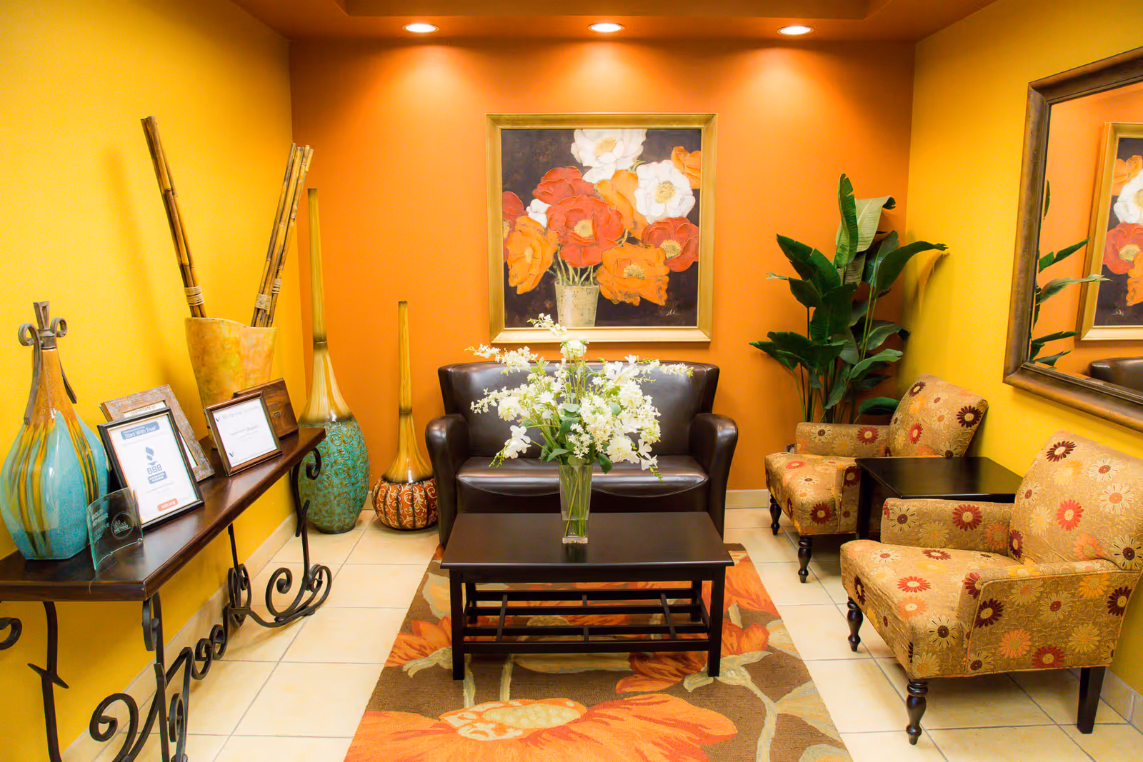 Bright yellow waiting area with sofa, armchairs, coffee table, plants, and wall art.