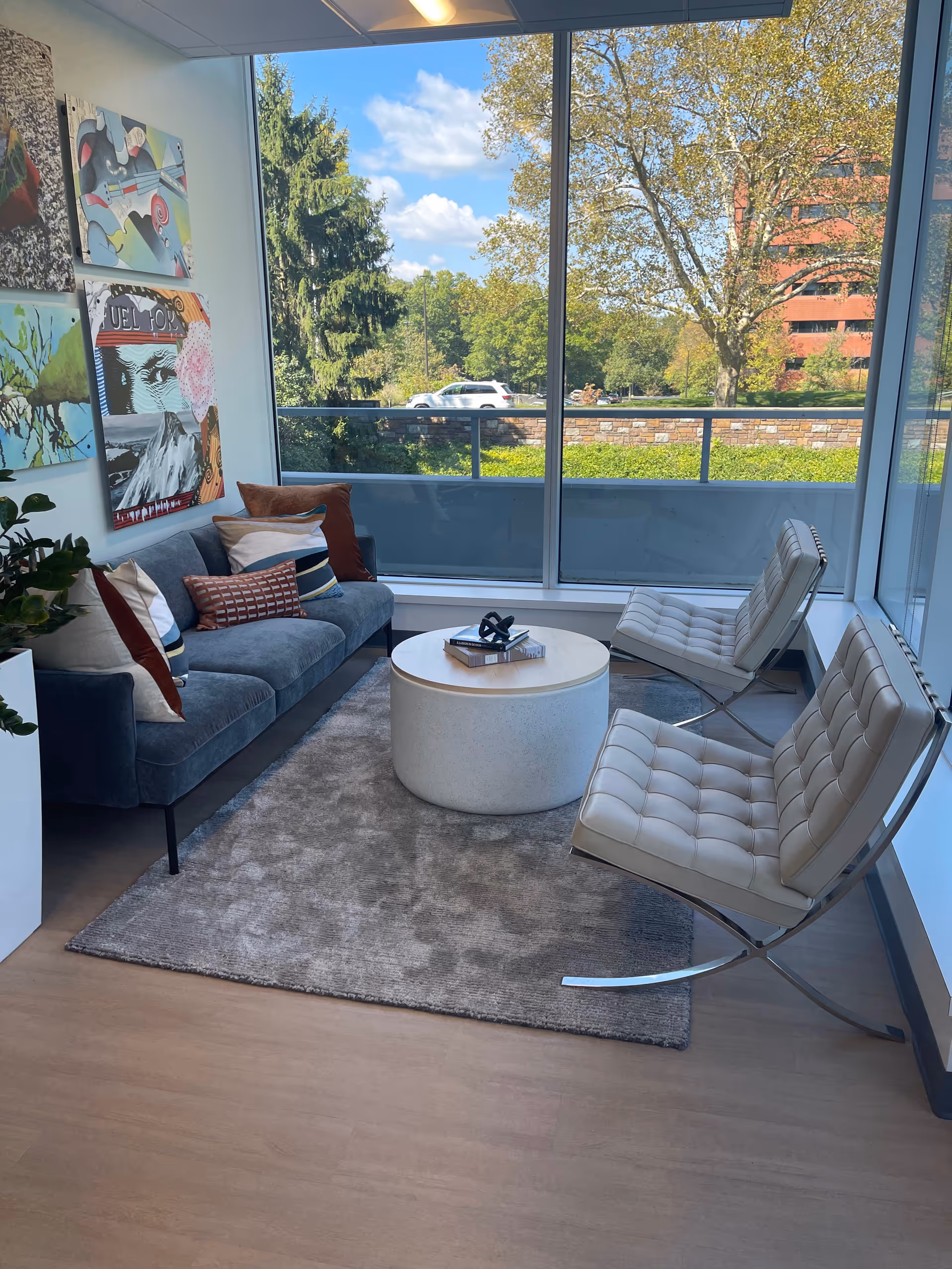 Modern lounge with blue sofa, white chairs, round coffee table, and large windows.