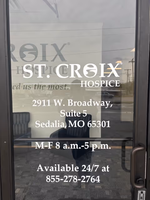Glass front door displays St. Croix Hospice name, address, and hours, with reflections.