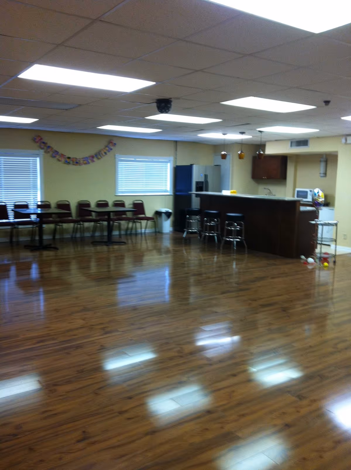 Spacious indoor common area with chairs along a wall and a bar-style kitchen counter with stools.