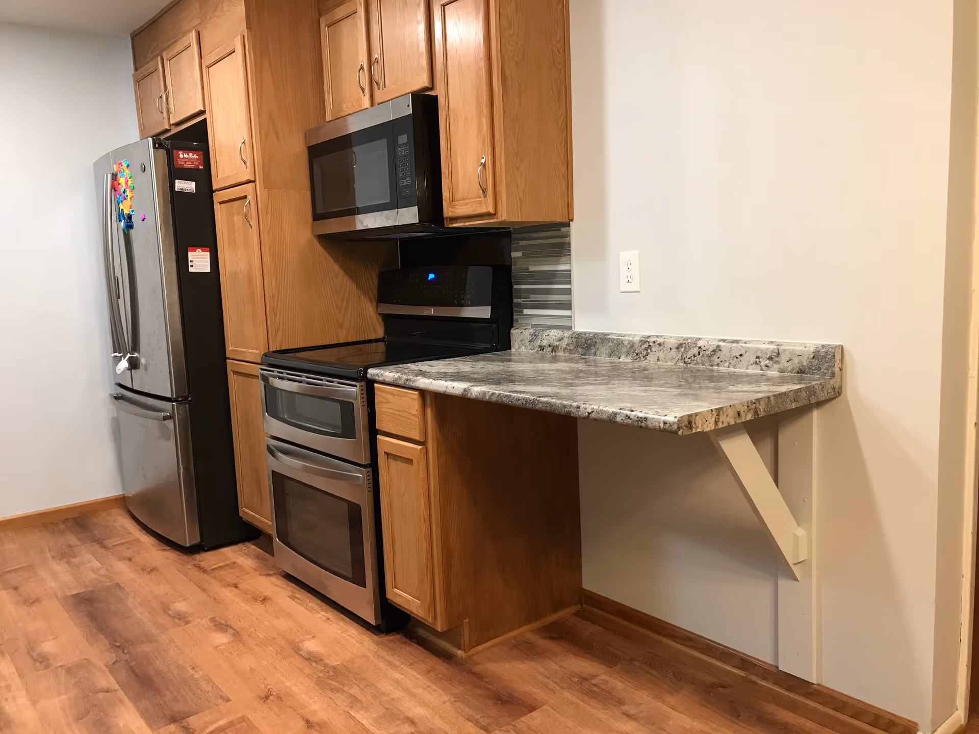 Kitchen area with stainless steel fridge and range, wooden cabinets, granite counter.