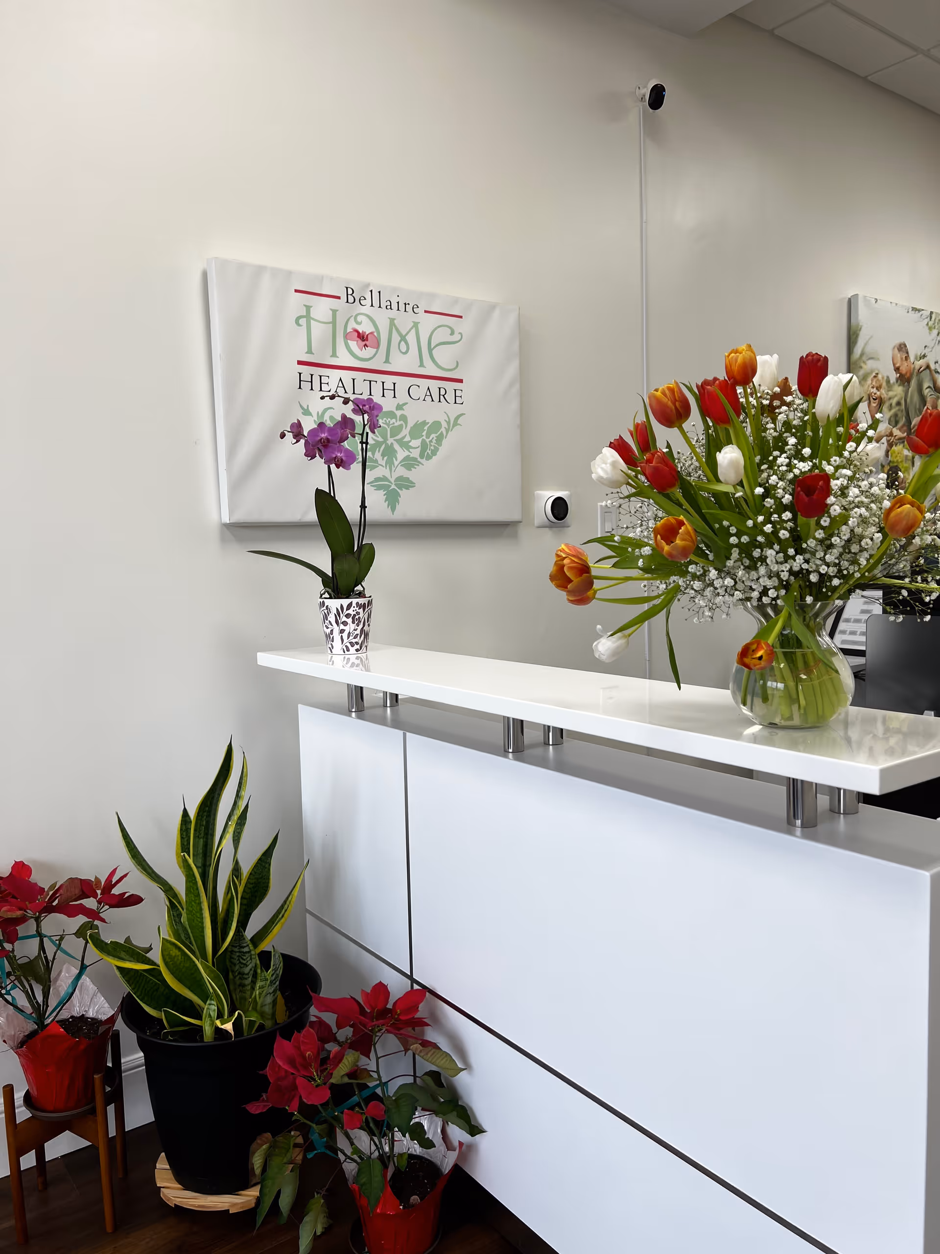 Reception area with white counter, potted plants, and a Bellaire Home Health Care sign.