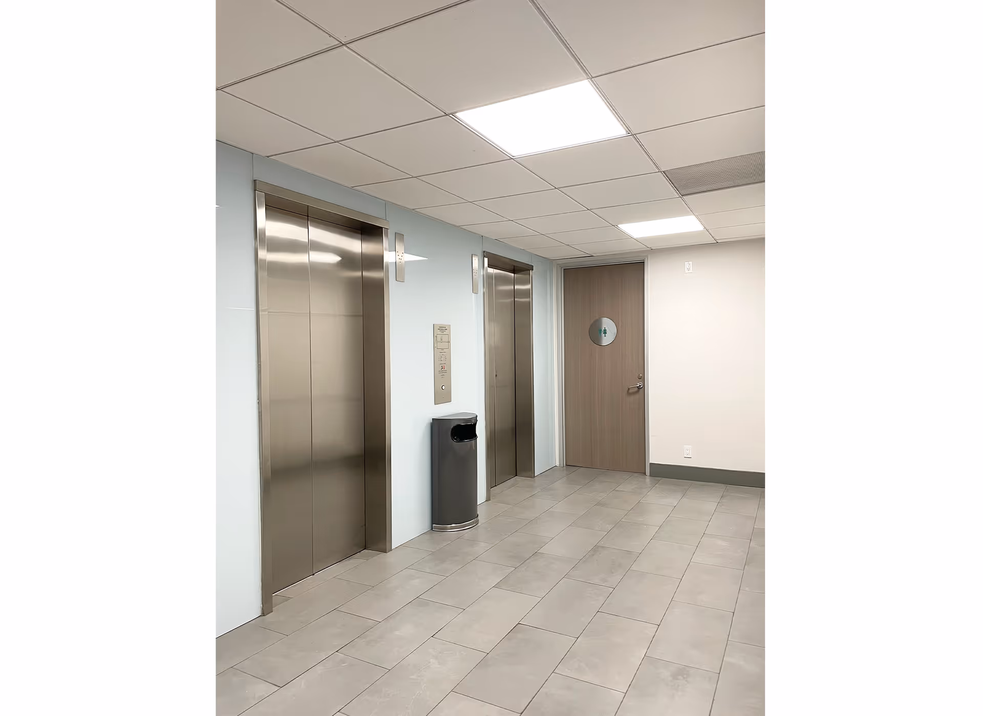 Interior hallway featuring two elevators, a trash can, and a wooden door.
