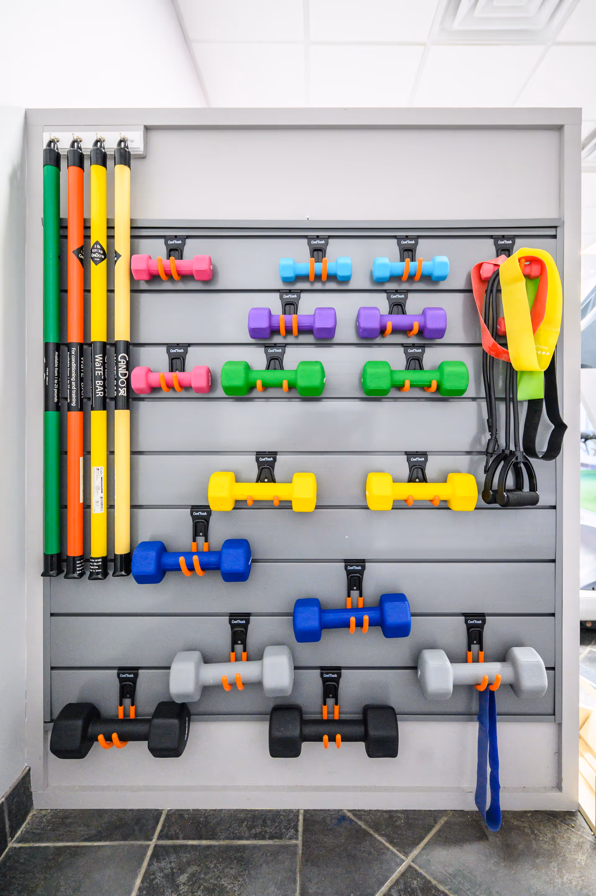 Wall-mounted rack with colorful dumbbells, resistance bands, and straps in a gym.