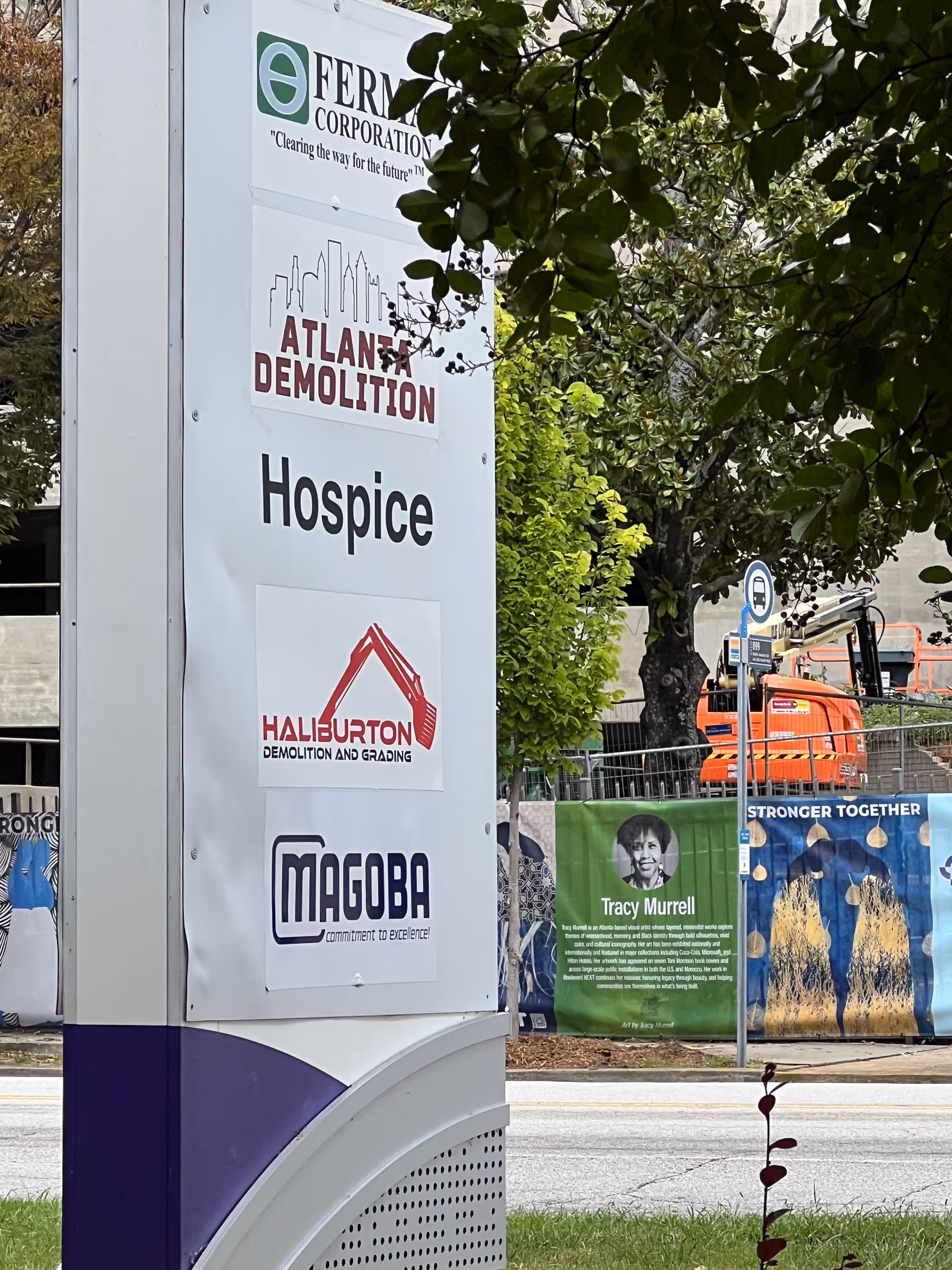 Outdoor signpost with hospice branding and contractor logos beside a construction site.