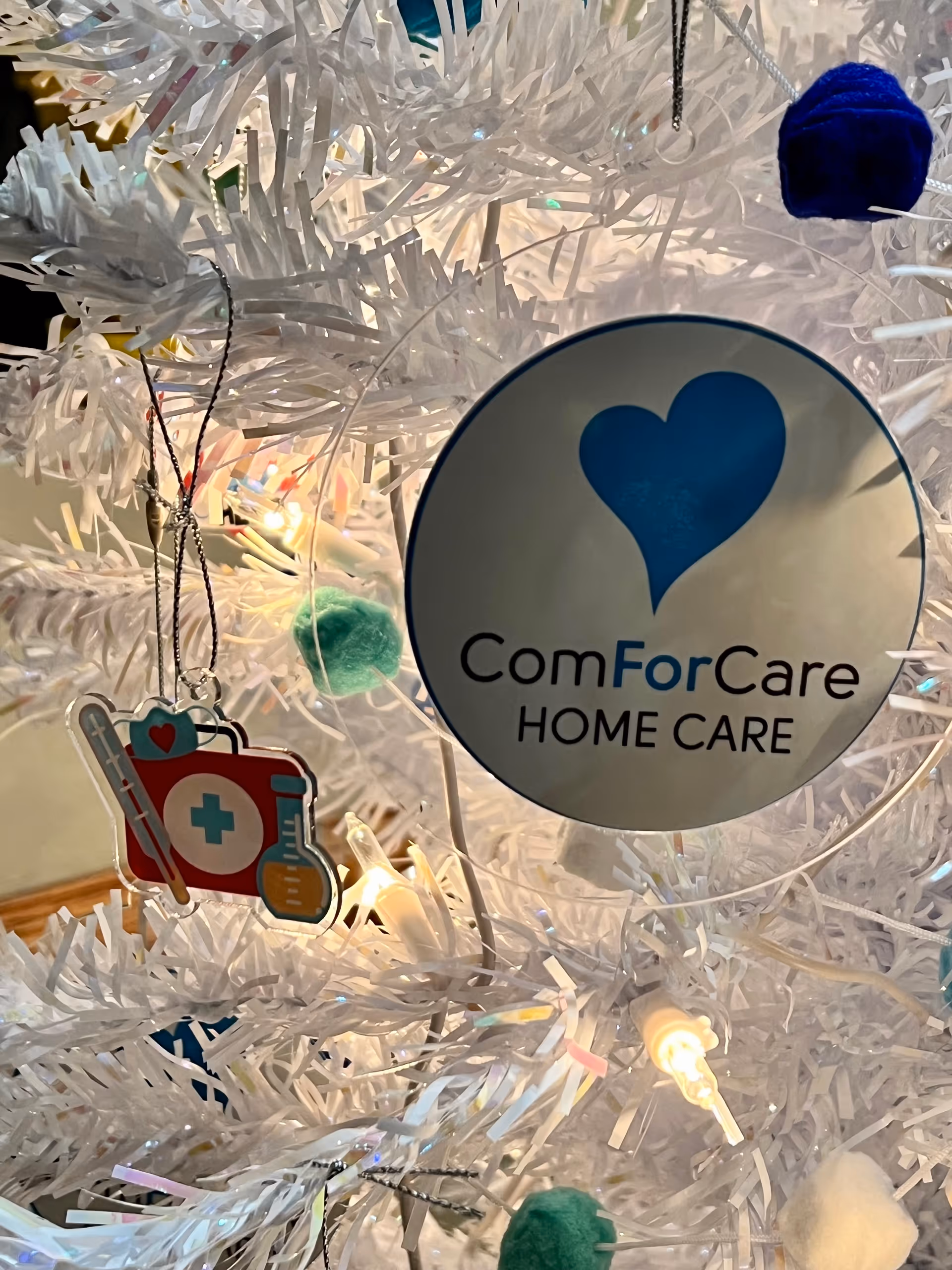 White Christmas tree with a ComForCare Home Care ornament and medical icons.