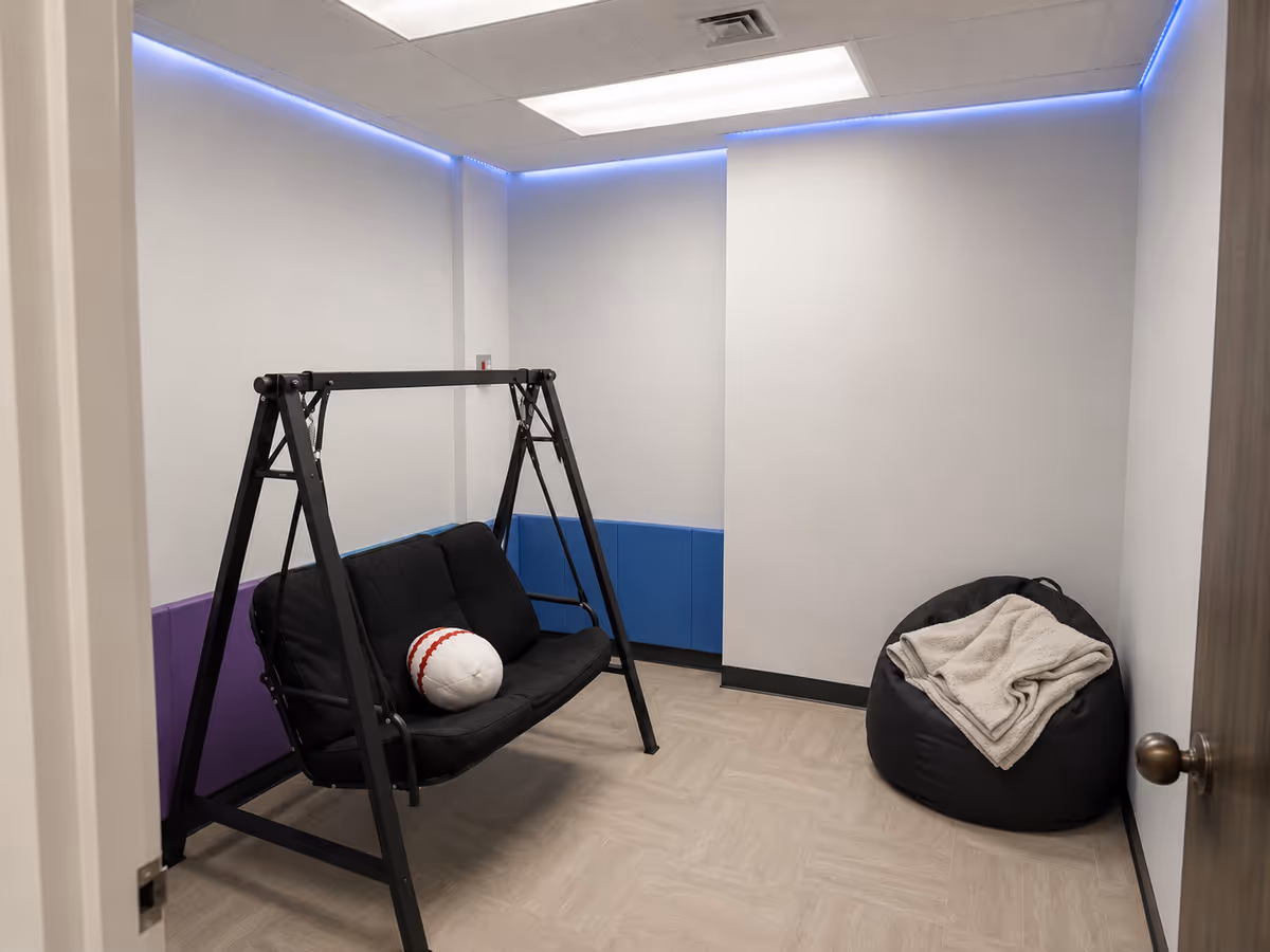 Interior activity room with a black metal swing, bean bag, and blue padded wall.
