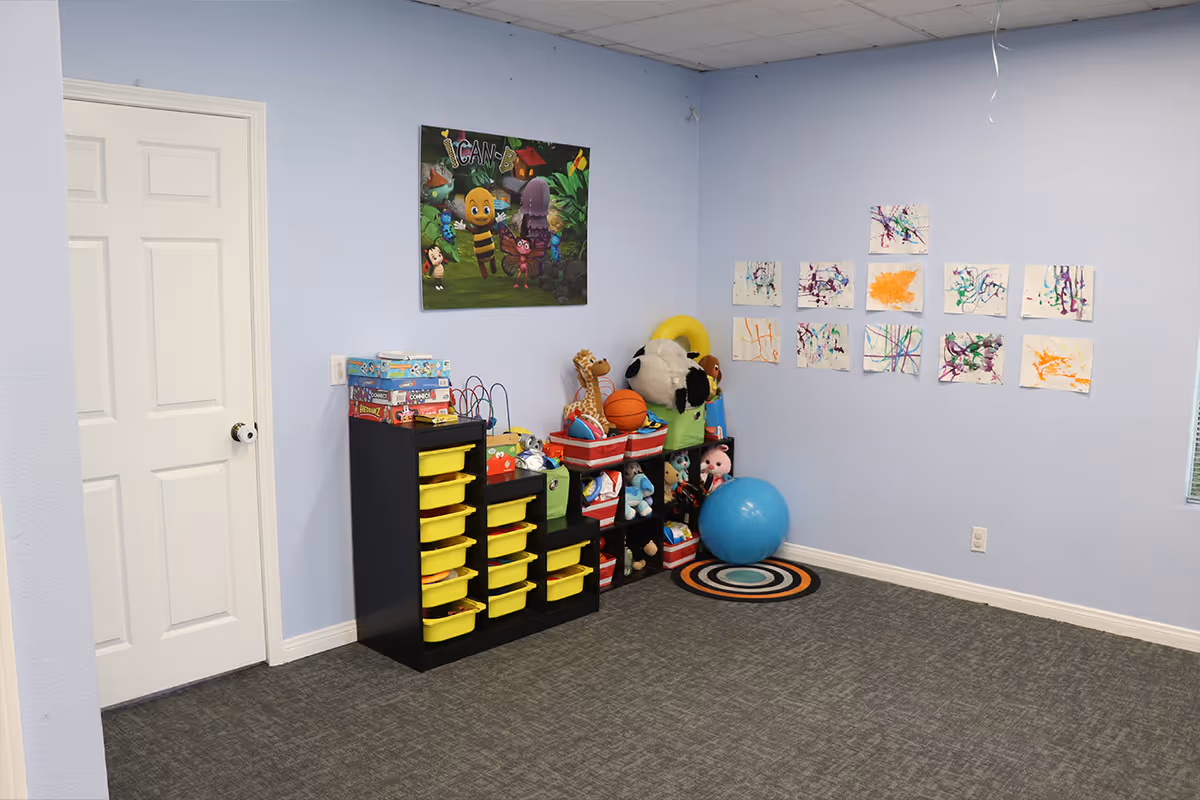 Blue-walled indoor playroom with toys, storage shelves, and children's artwork.