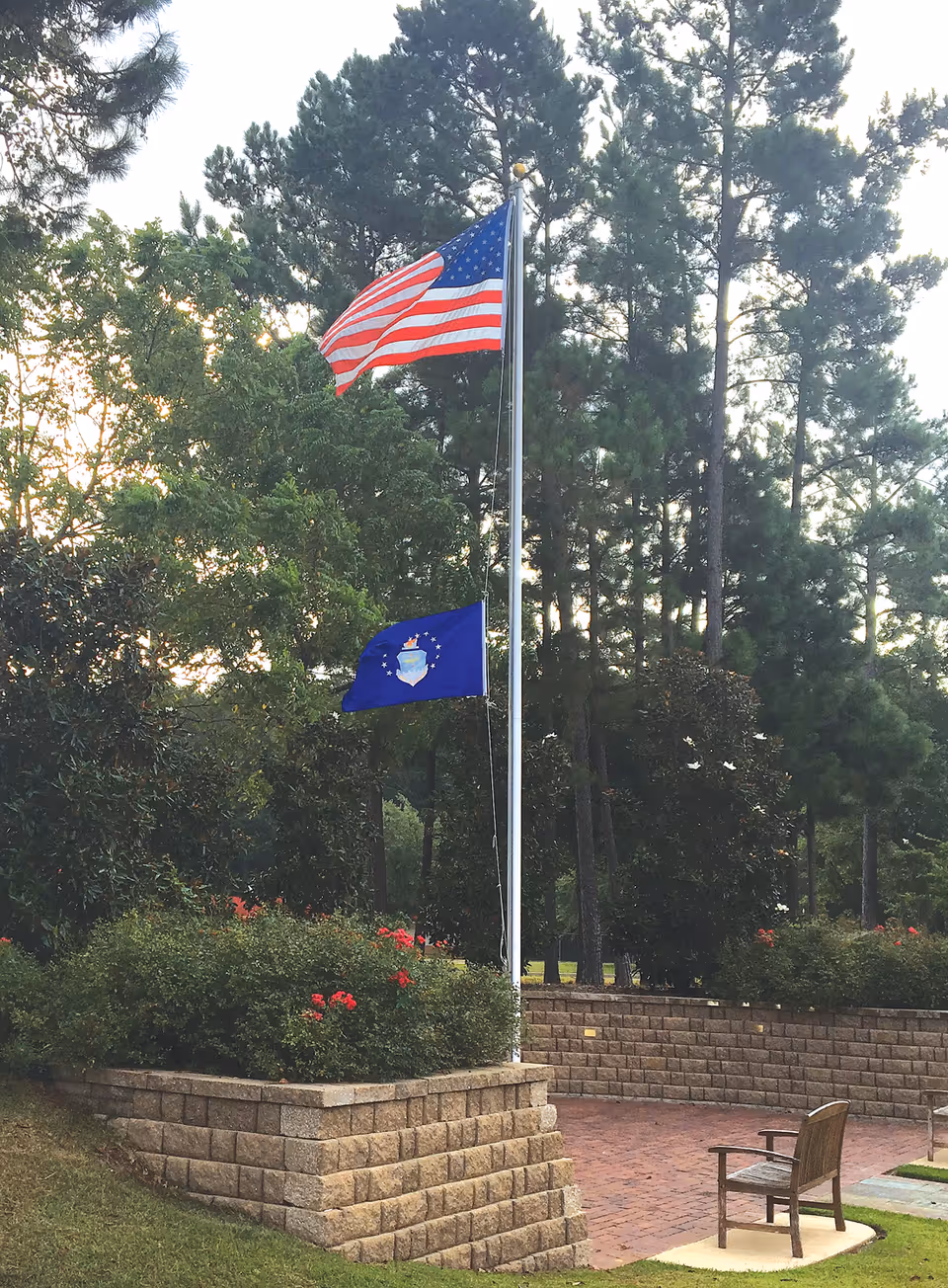 American flag and blue flag on flagpoles beside a brick garden area.