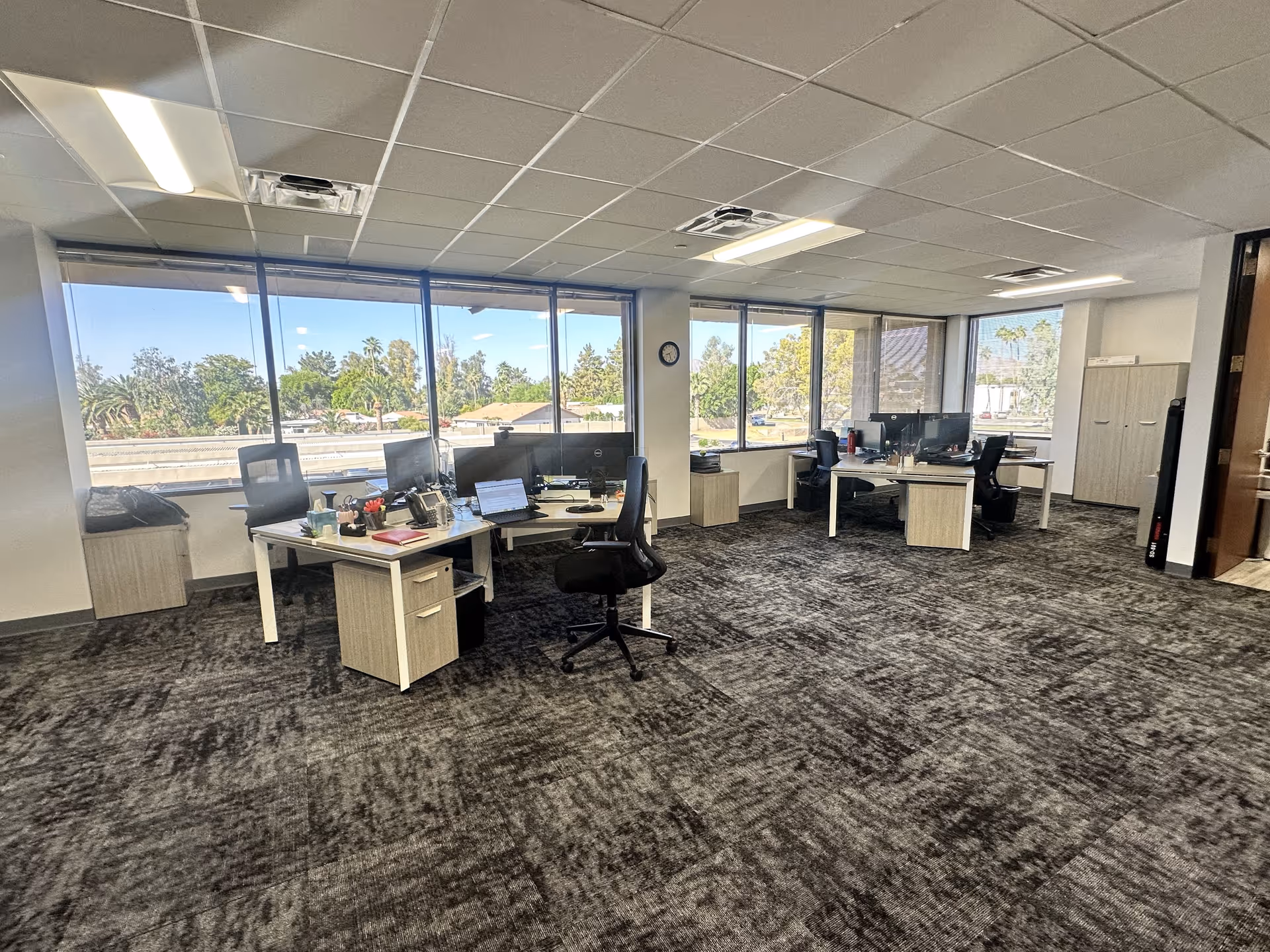 Open office space with desks, computers, and expansive windows overlooking outdoors.