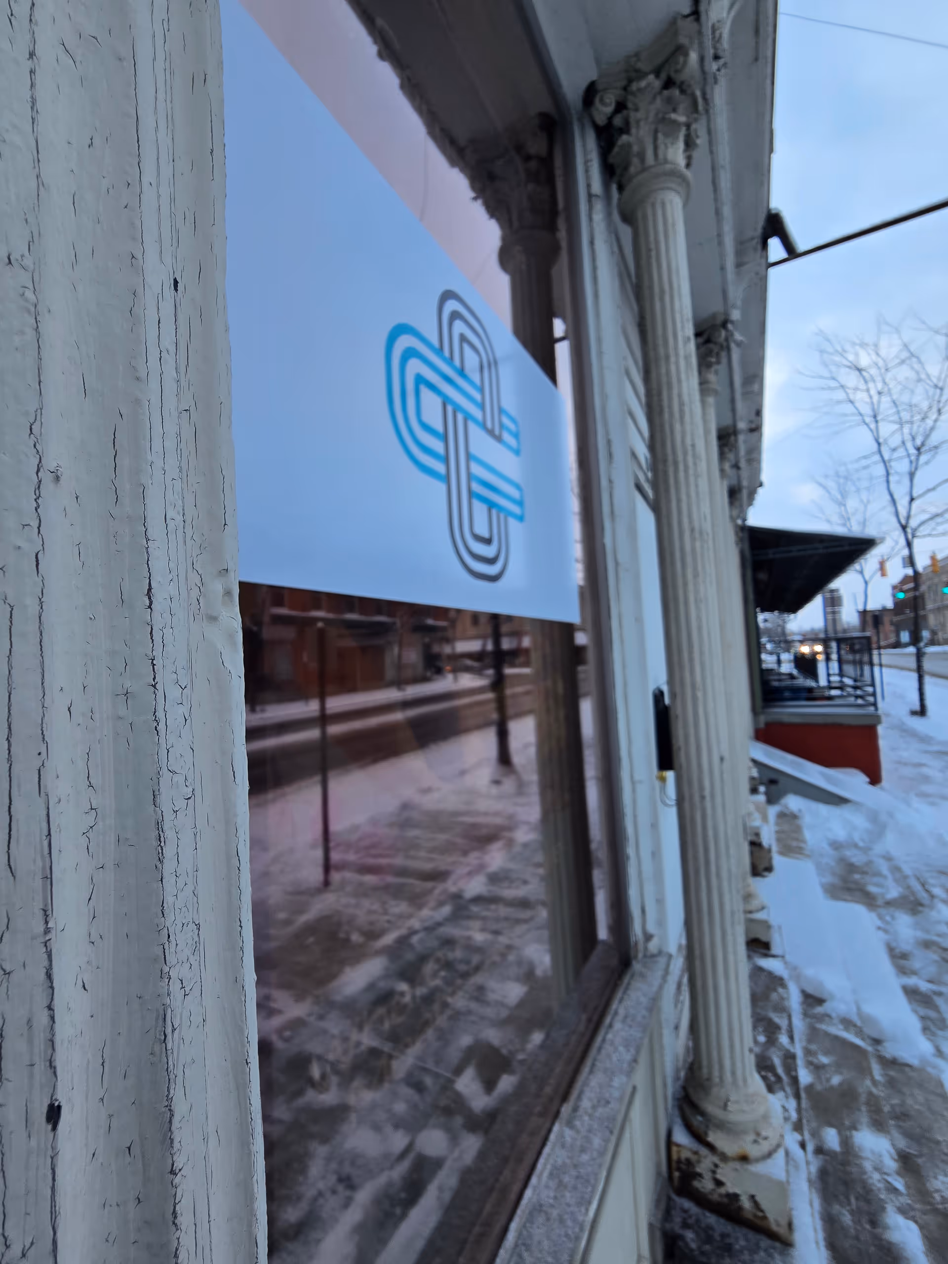 Front of a building with a decorative sign and columns along a snowy street.