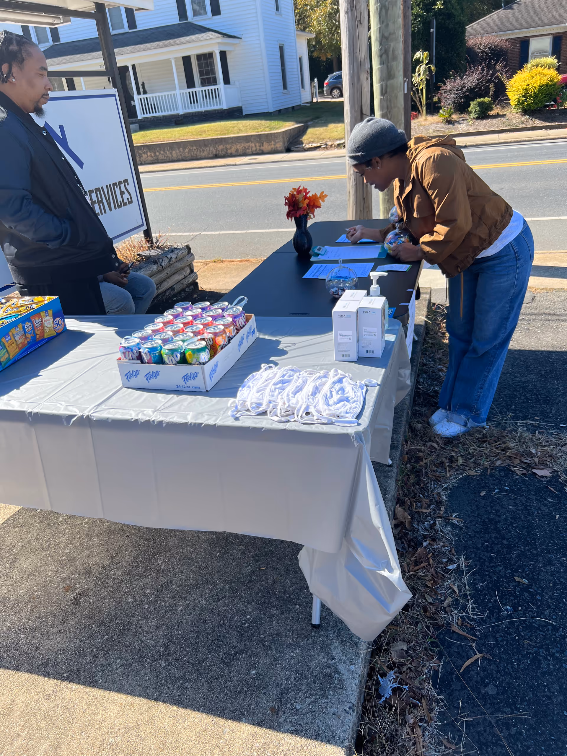 Two people at an outdoor information table outside a senior care facility signing paperwork.