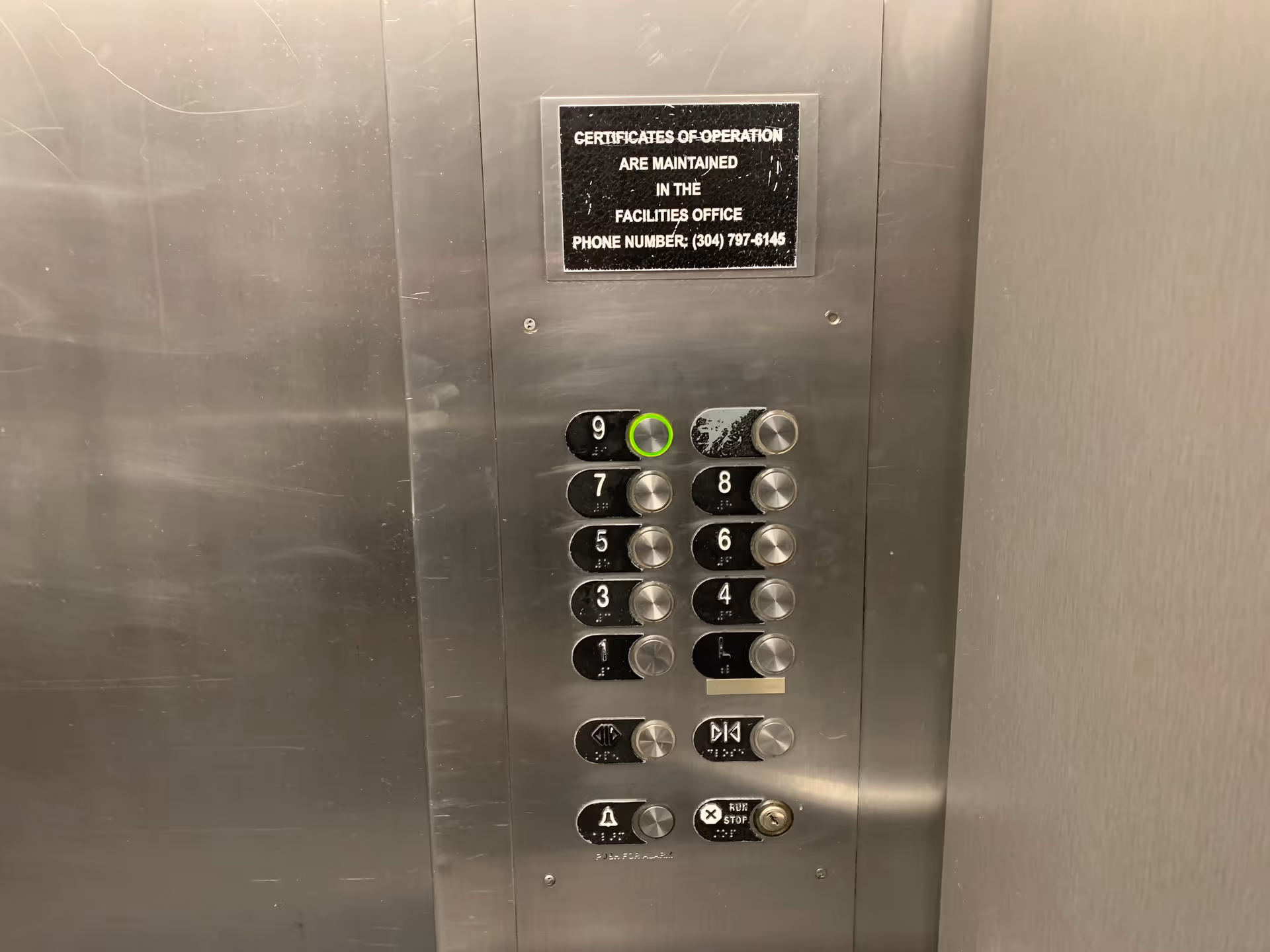 Interior elevator panel with numbered floor buttons and a maintenance note plaque.