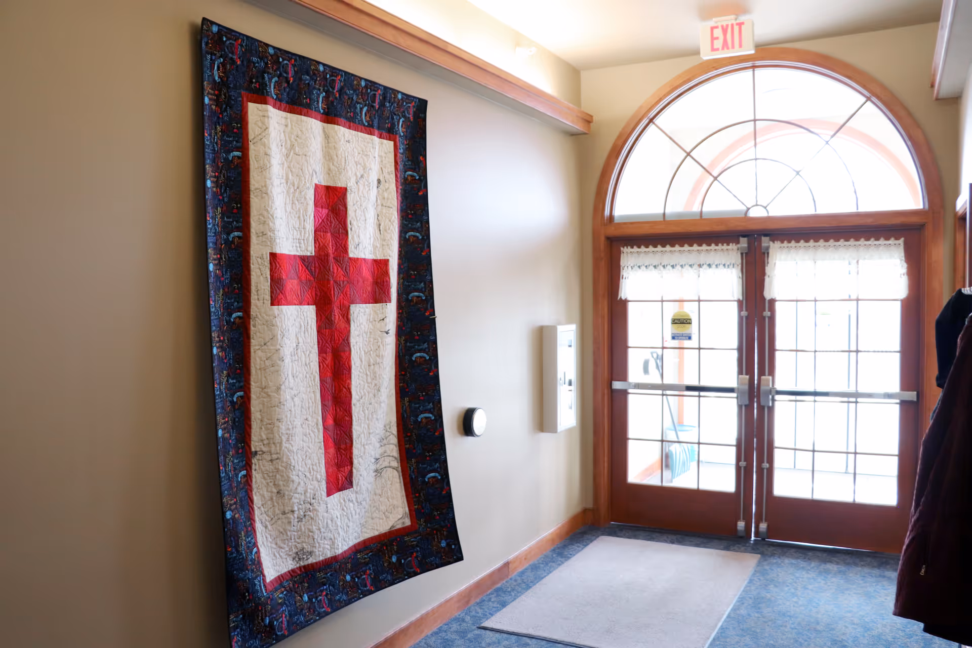 Hallway interior with a quilt displaying a red cross beside glass double doors.