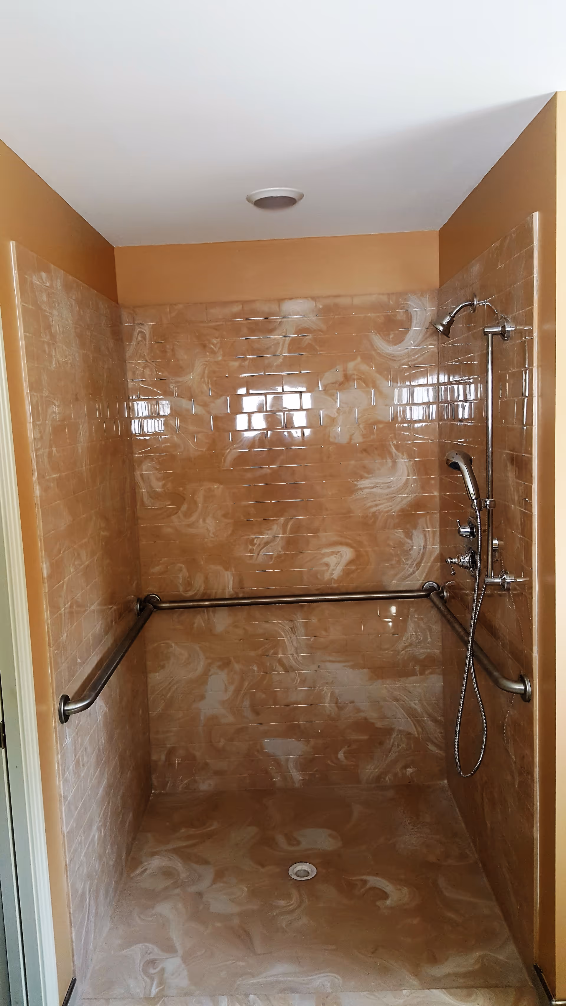 Beige-tiled roll-in shower with grab bars on walls and a handheld shower head.