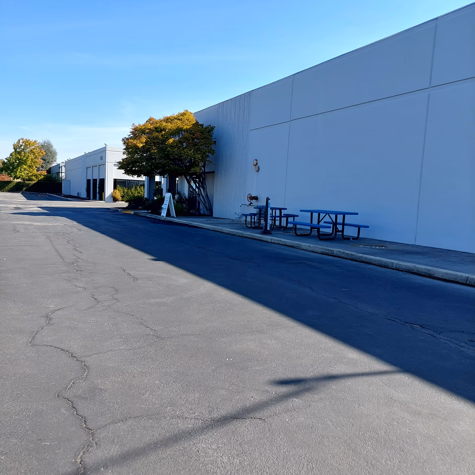 Exterior view of a large white facility with blue picnic tables along the sidewalk.