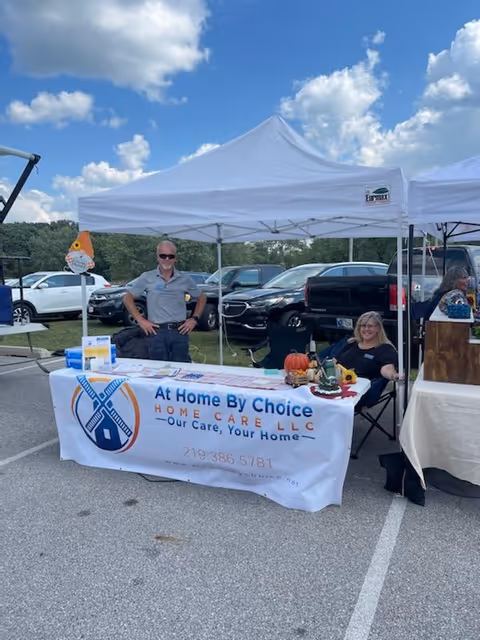 Two staff members man a booth promoting At Home By Choice Home Care LLC under tents.
