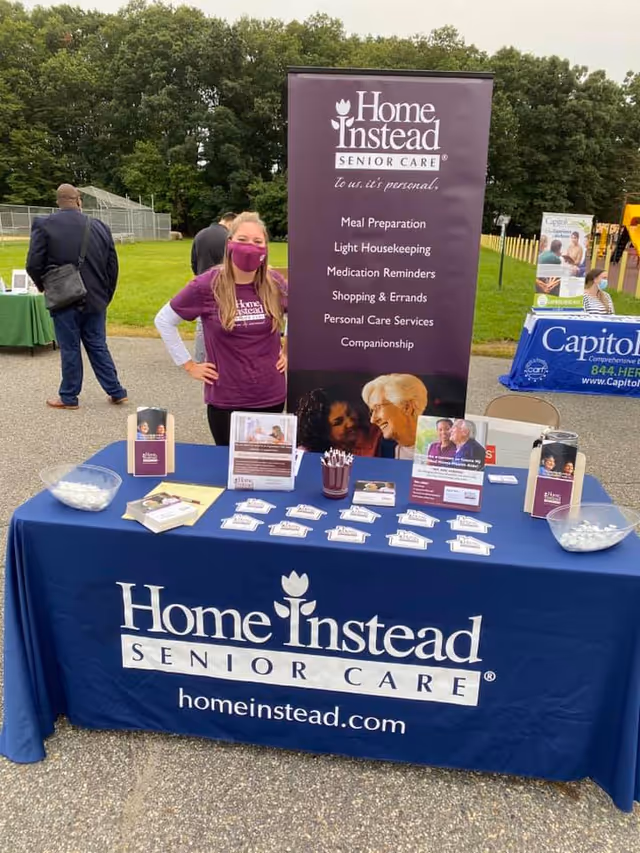 Promotional Home Instead Senior Care booth outdoors with banner and table.