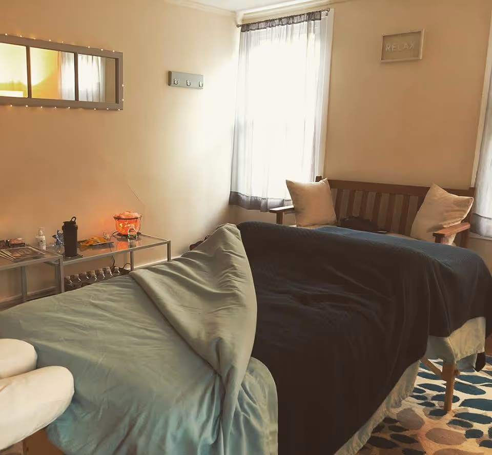 A cozy massage/therapy room with a table, chairs, and soft lighting.