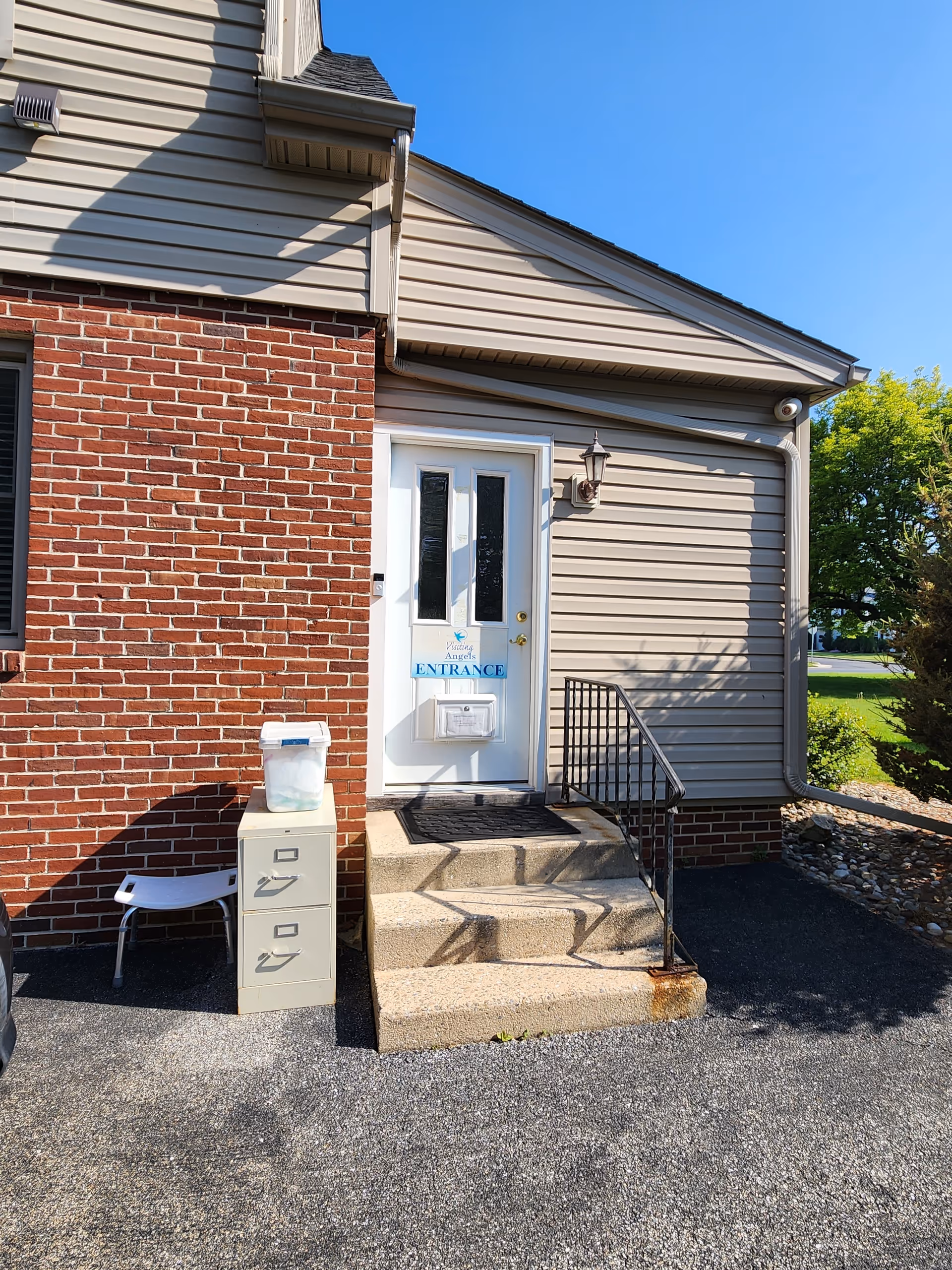 Exterior view of a senior home entrance with brick wall, stairs, railing, and blue sky.
