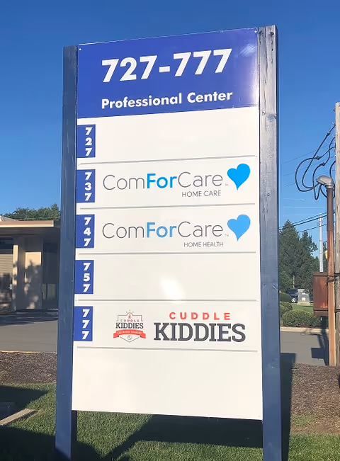 Tall outdoor signboard with ComForCare logos and phone number in front of facility.