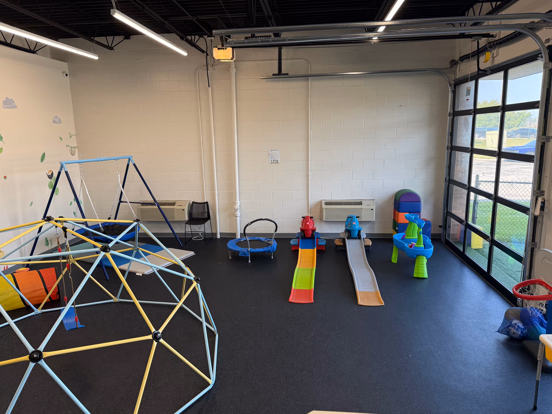 Indoor playroom with colorful climbing structure, slide ramps, and children's toys for therapy sessions.