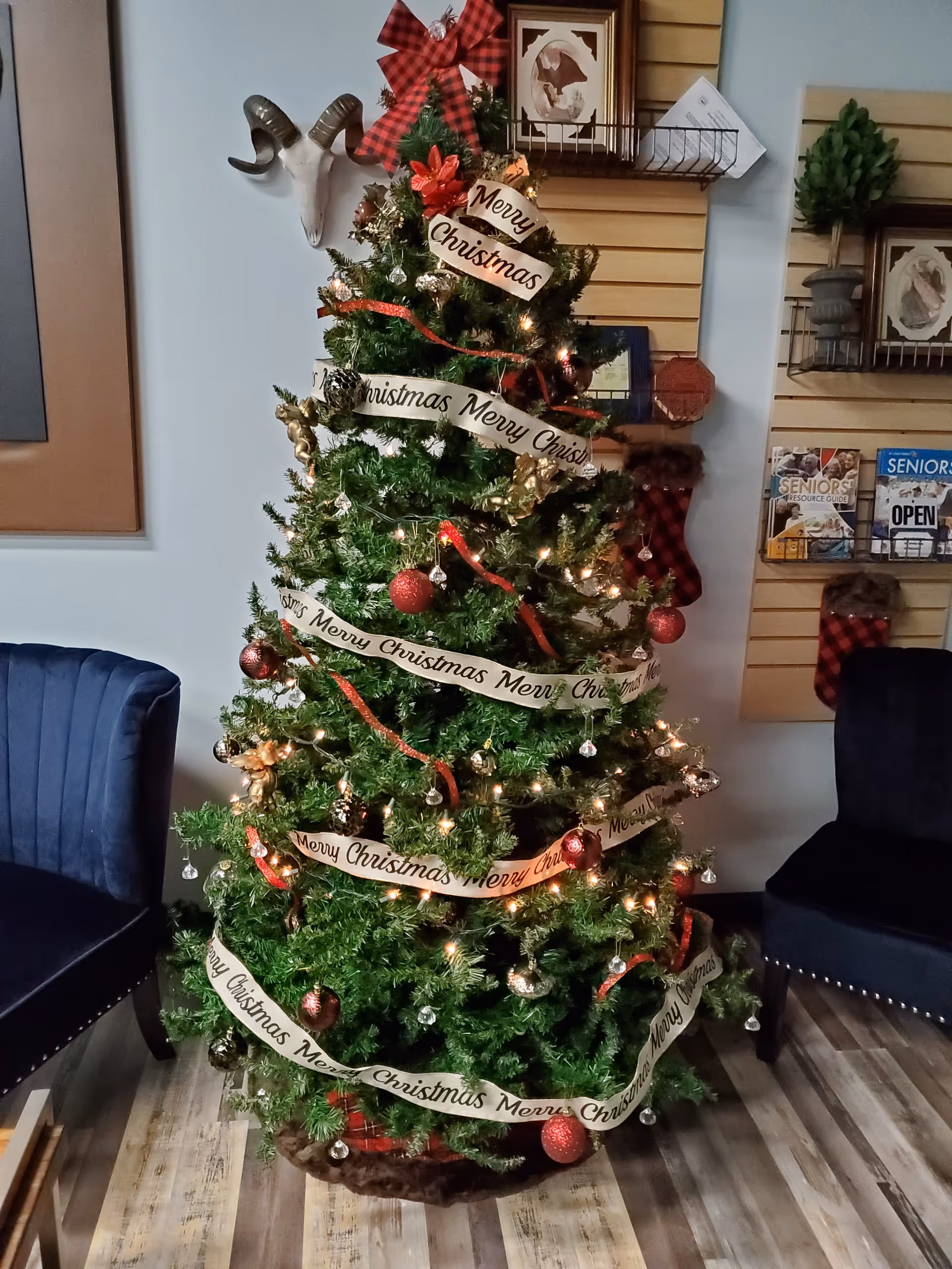 Decorated Christmas tree with 'Merry Christmas' ribbons in a cozy indoor lobby.