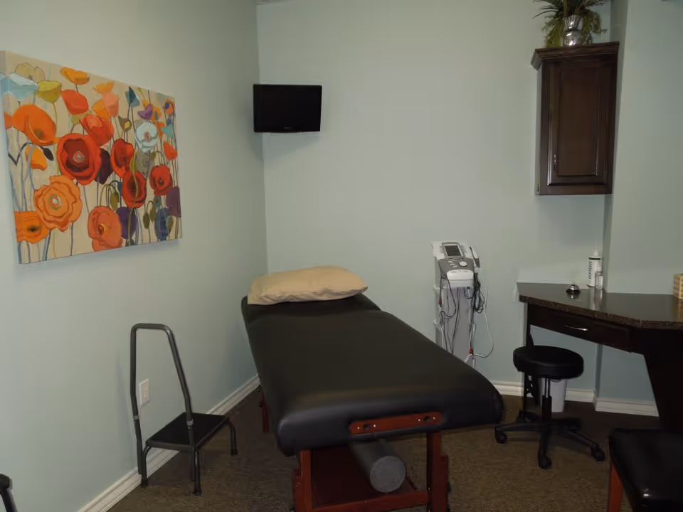 Examination room with a treatment bed, equipment, desk, and colorful wall art.