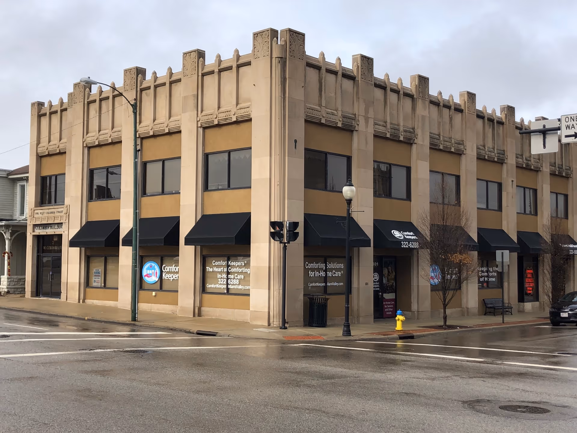 Street-level view of a beige multi-story building with Comfort Keepers storefronts.