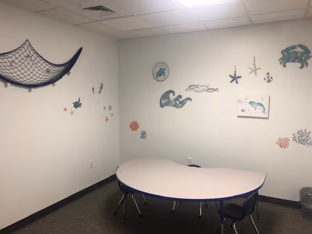 An interior activity room with seashell decals, a curved table, and small chairs.