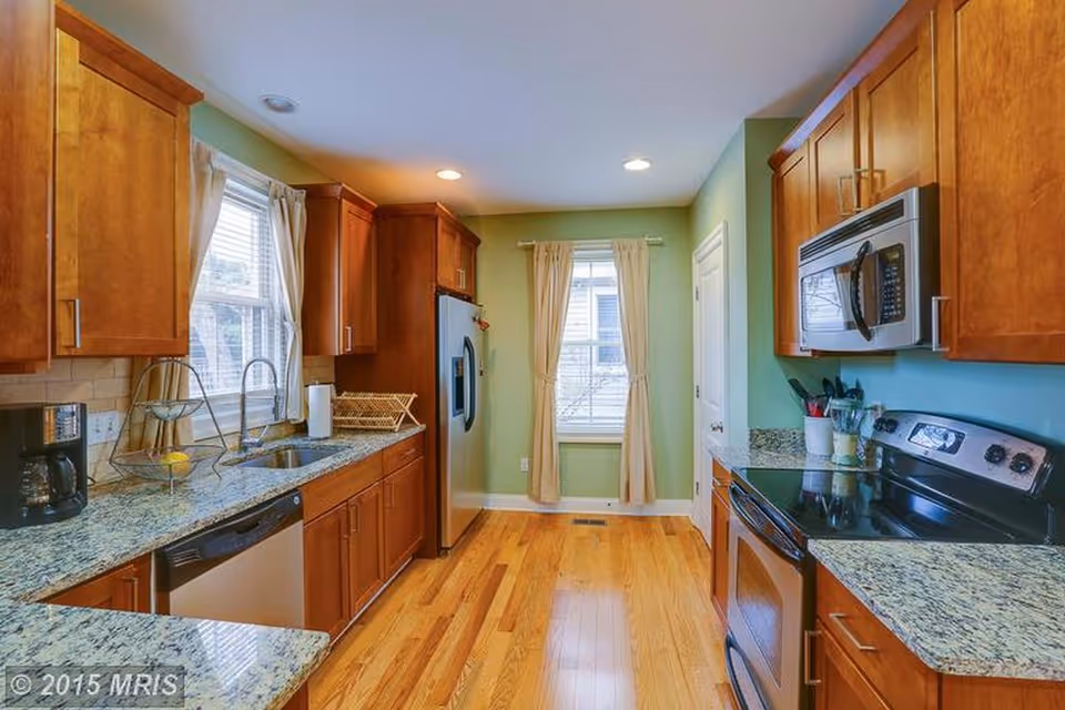 Bright kitchen with wooden cabinets, granite countertops, stainless appliances, and wood floors.
